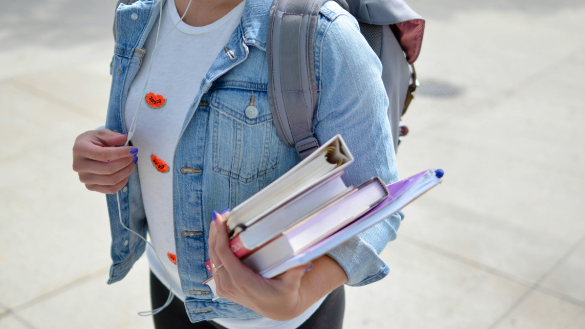 A student walking with a backpack and books