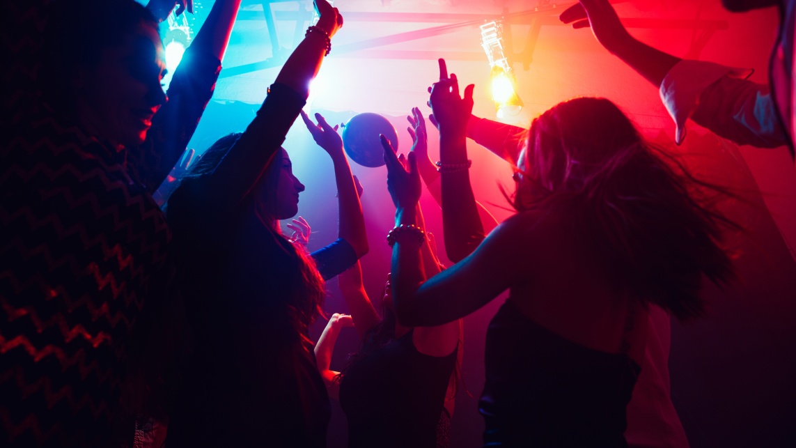 A group of people at dark but vividly lit nightclub with blue, red, purple, and yellow lighting. 